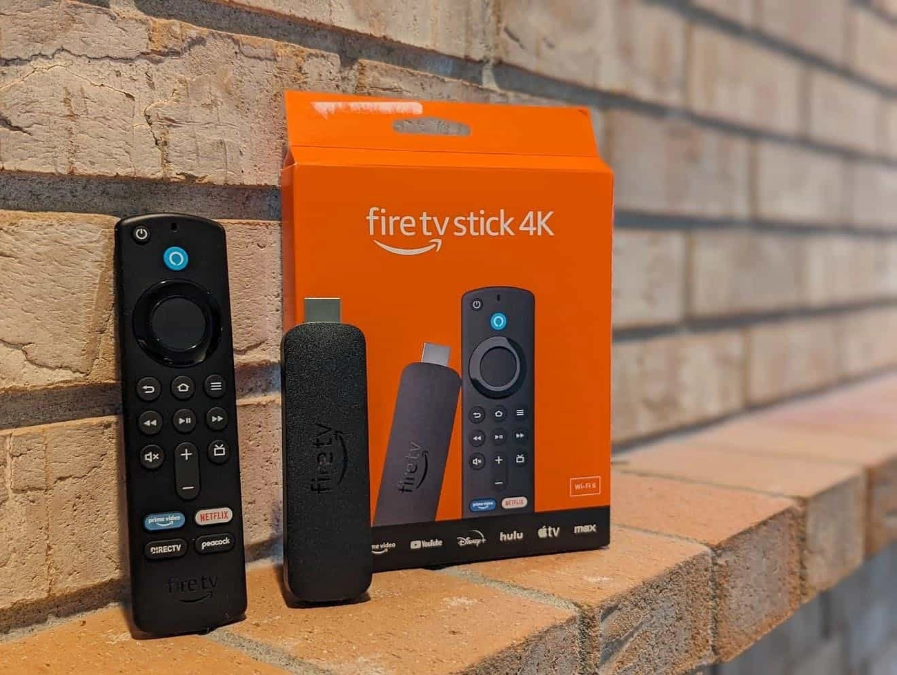 Amazon Fire TV Stick 4K with remote and packaging displayed on a brick ledge outdoors.